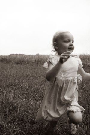 Black and white photos of baby in white dress crawling through grass.