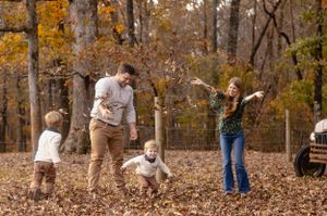 People playing and throwing autumn leaves in a wooded area during fall.