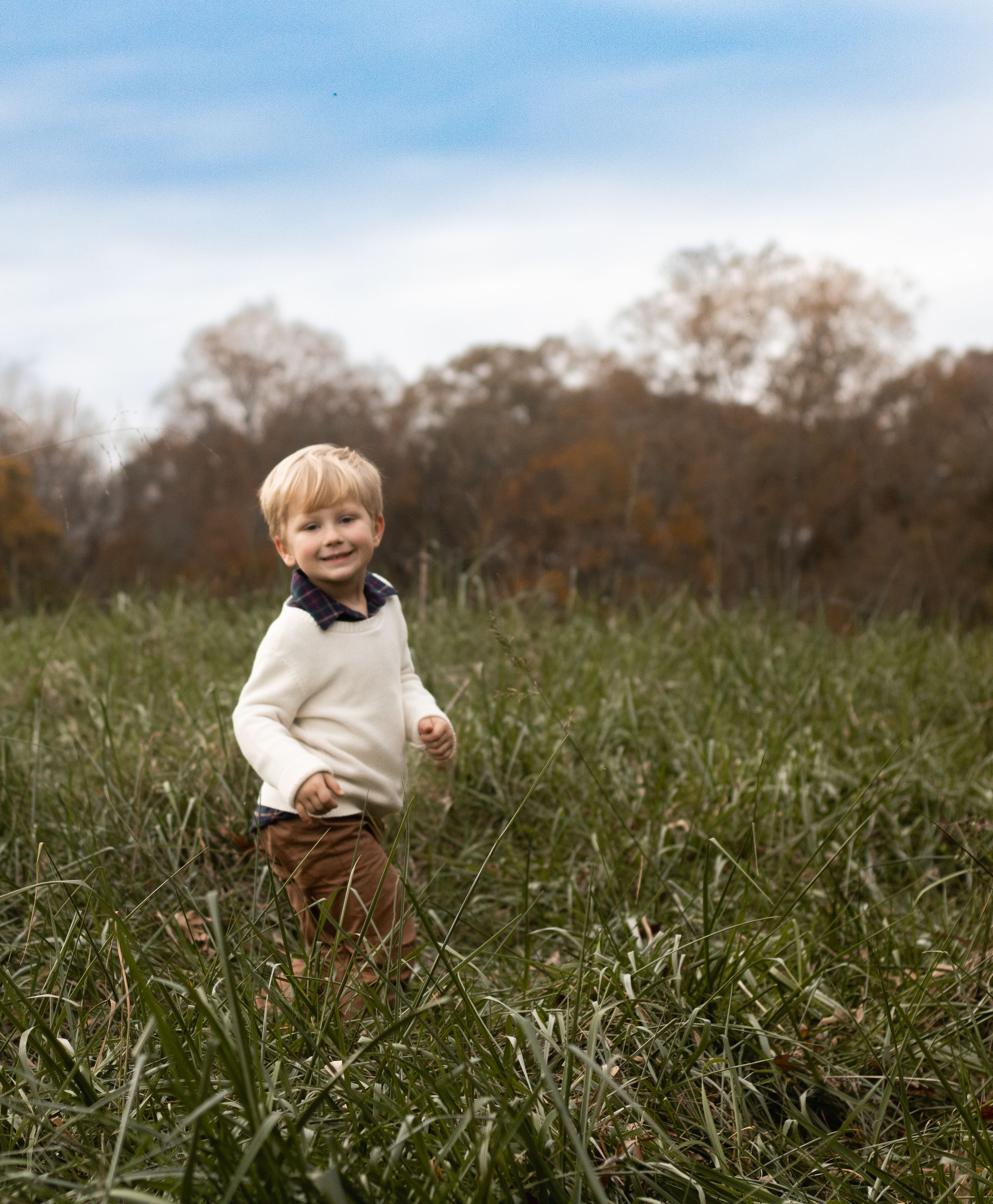 A small figure in a cream sweater walking through tall grass in a field.