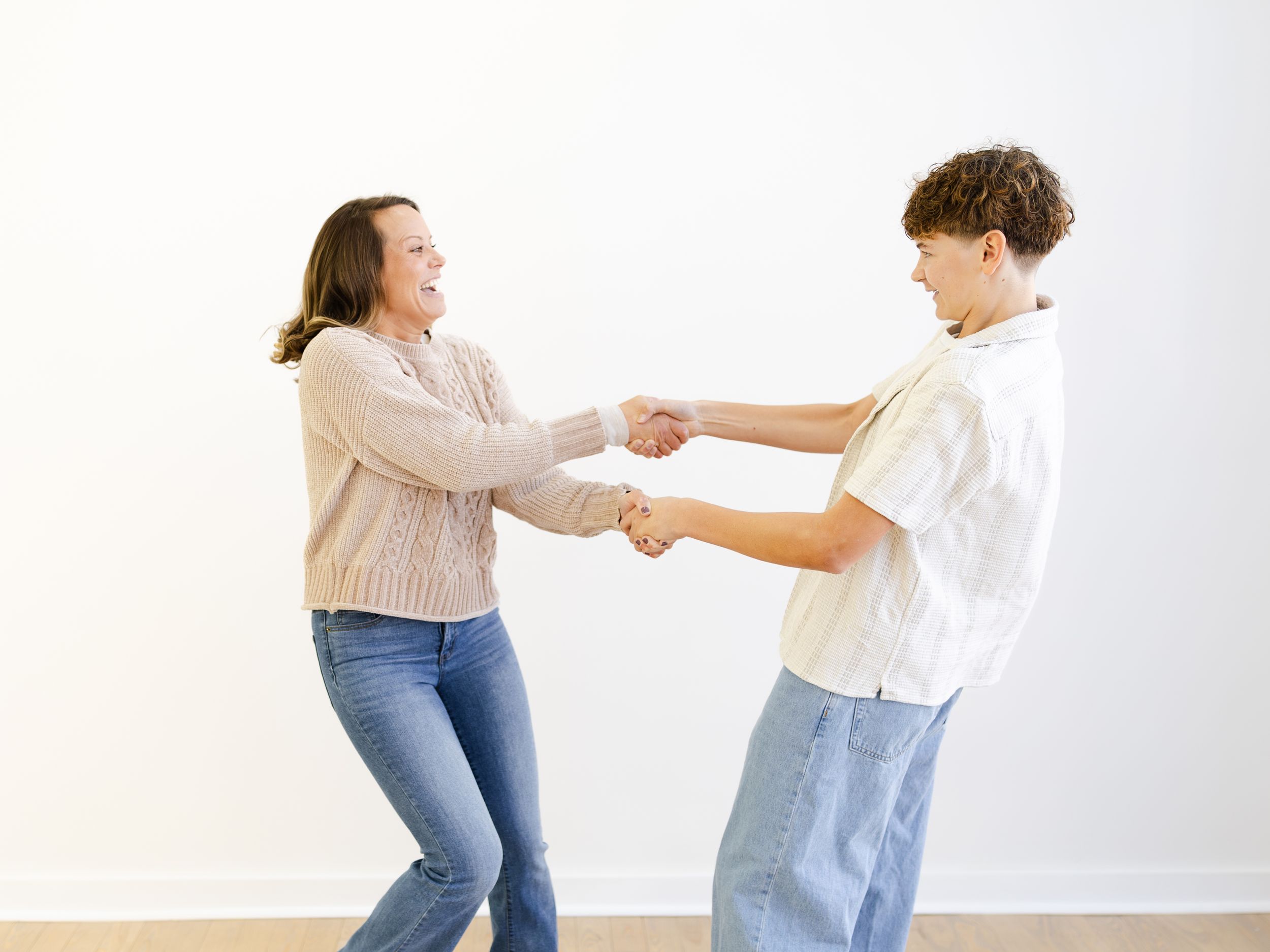 Two dancers in casual attire perform a dynamic swing dance move against a white background.