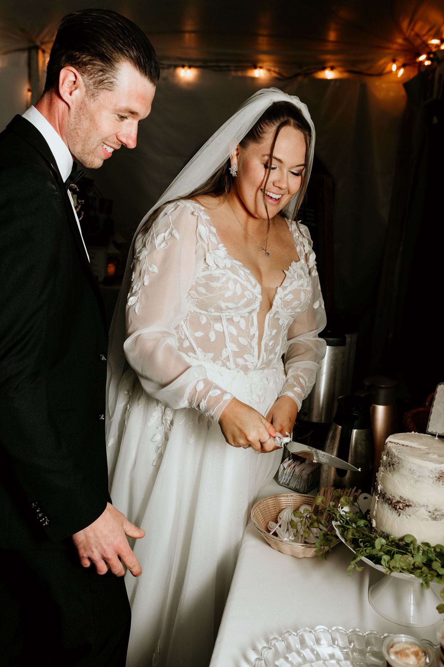 A couple in wedding attire shares an intimate moment while cutting their wedding cake in a dimly lit reception venue.