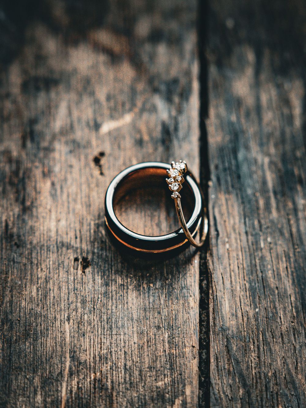 Wedding rings with a diamond solitaire engagement ring resting on rustic wooden surface in macro photography.