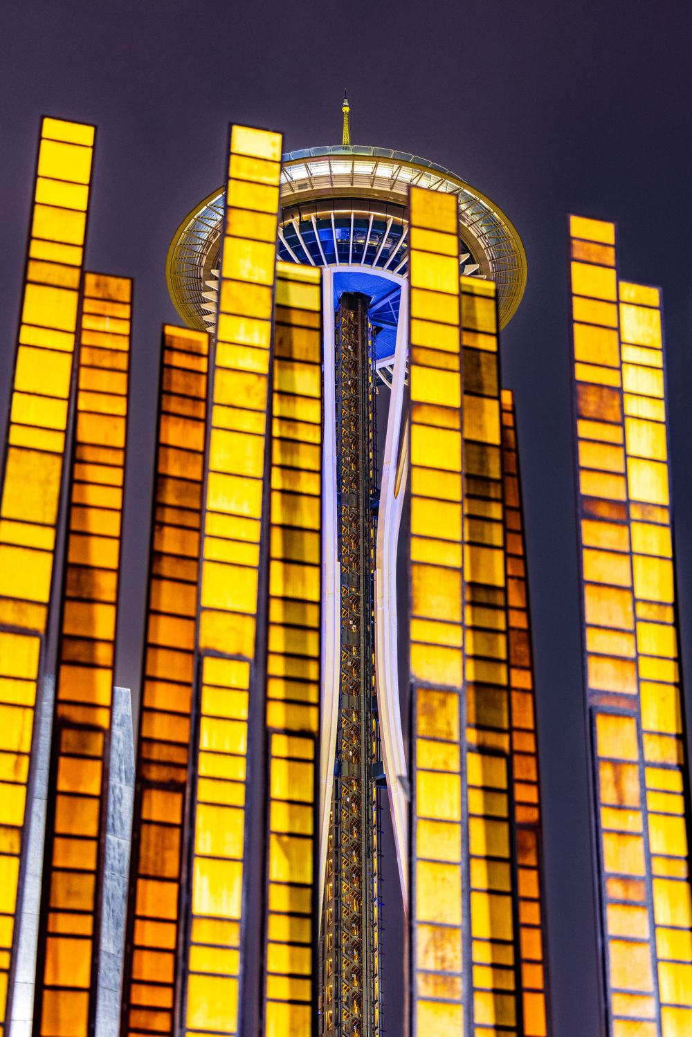 Illuminated yellow light pillars frame Seattle Space Needle at night.