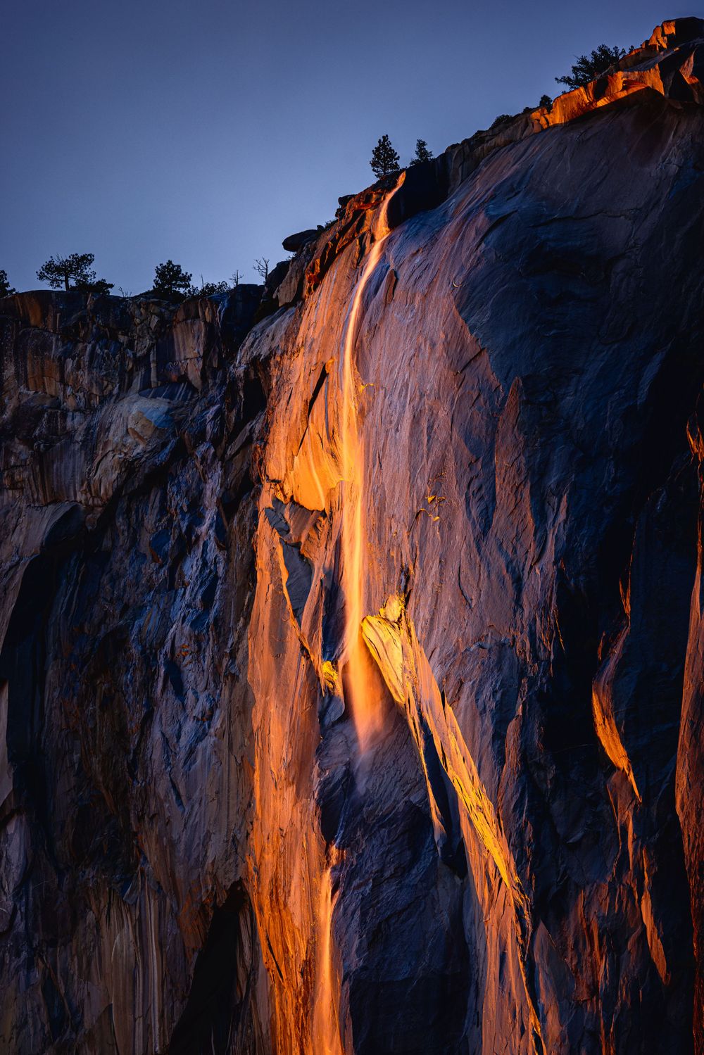 Glowing orange waterfall cascades down dark granite cliffs at dusk.