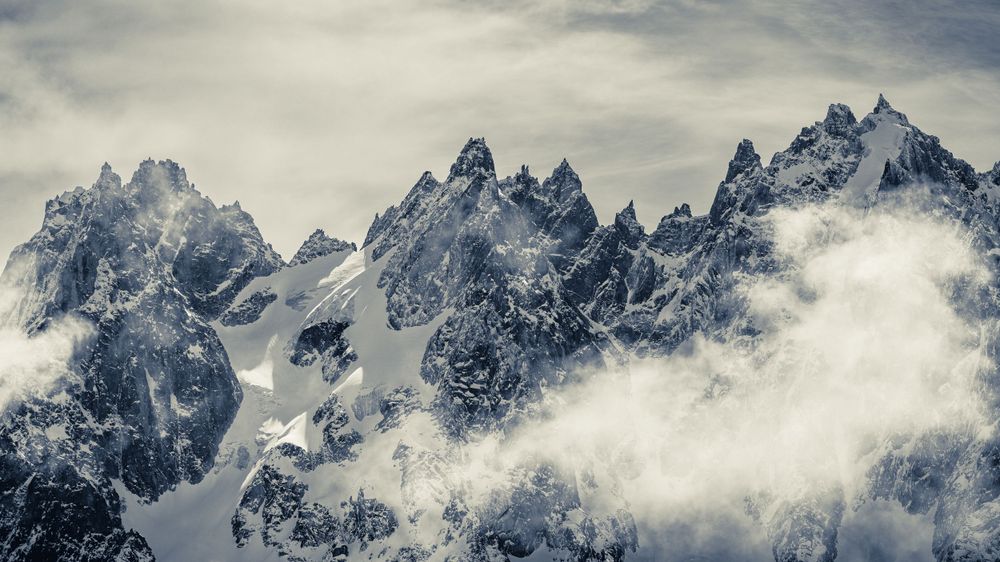 Jagged mountain peaks covered in snow with clouds swirling around the summits.