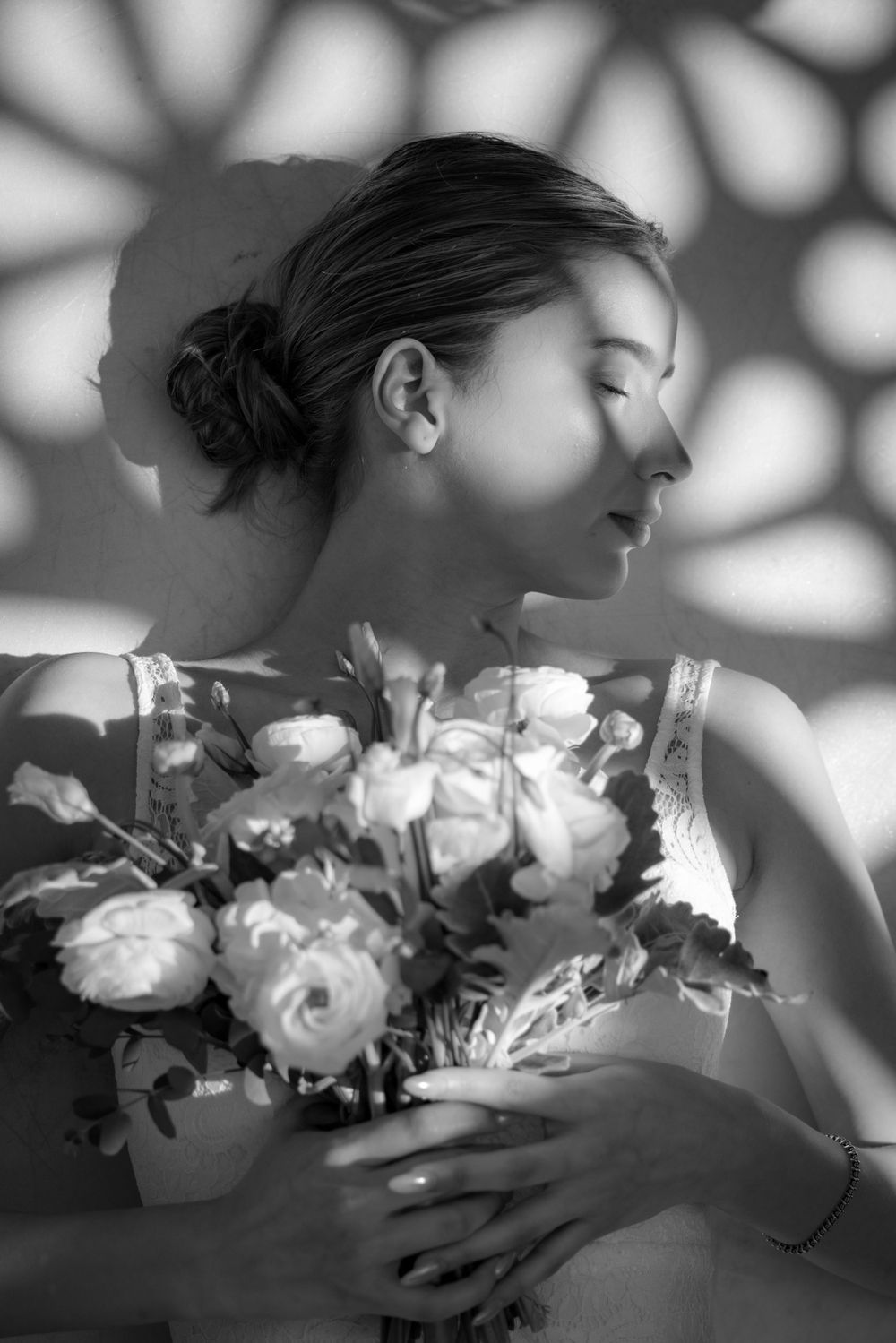 A black and white artistic photograph of a romantic side profile pose with white roses and dappled shadows.