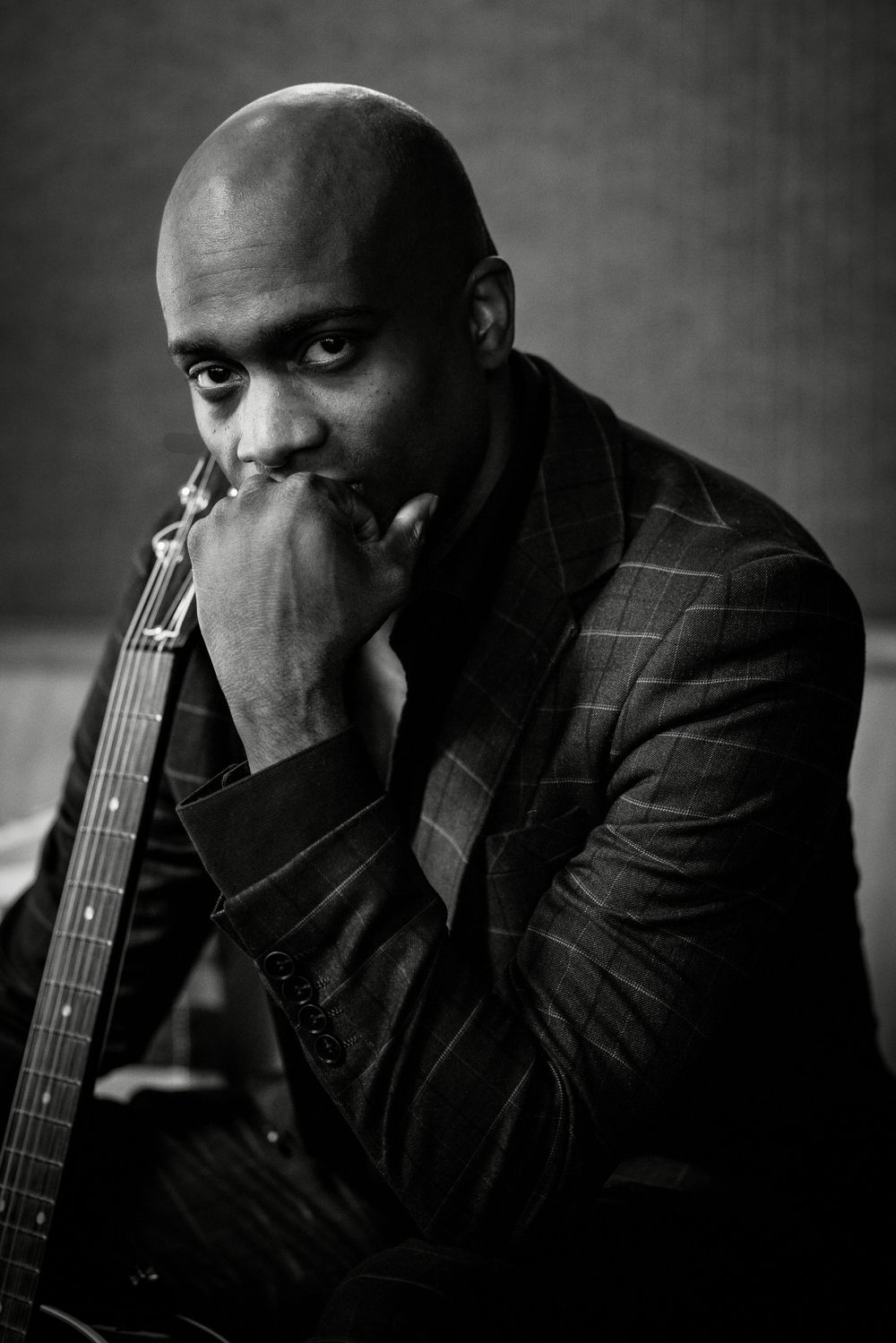 Black and white portrait of a pensive figure in a pinstripe suit leaning forward with hand near face.