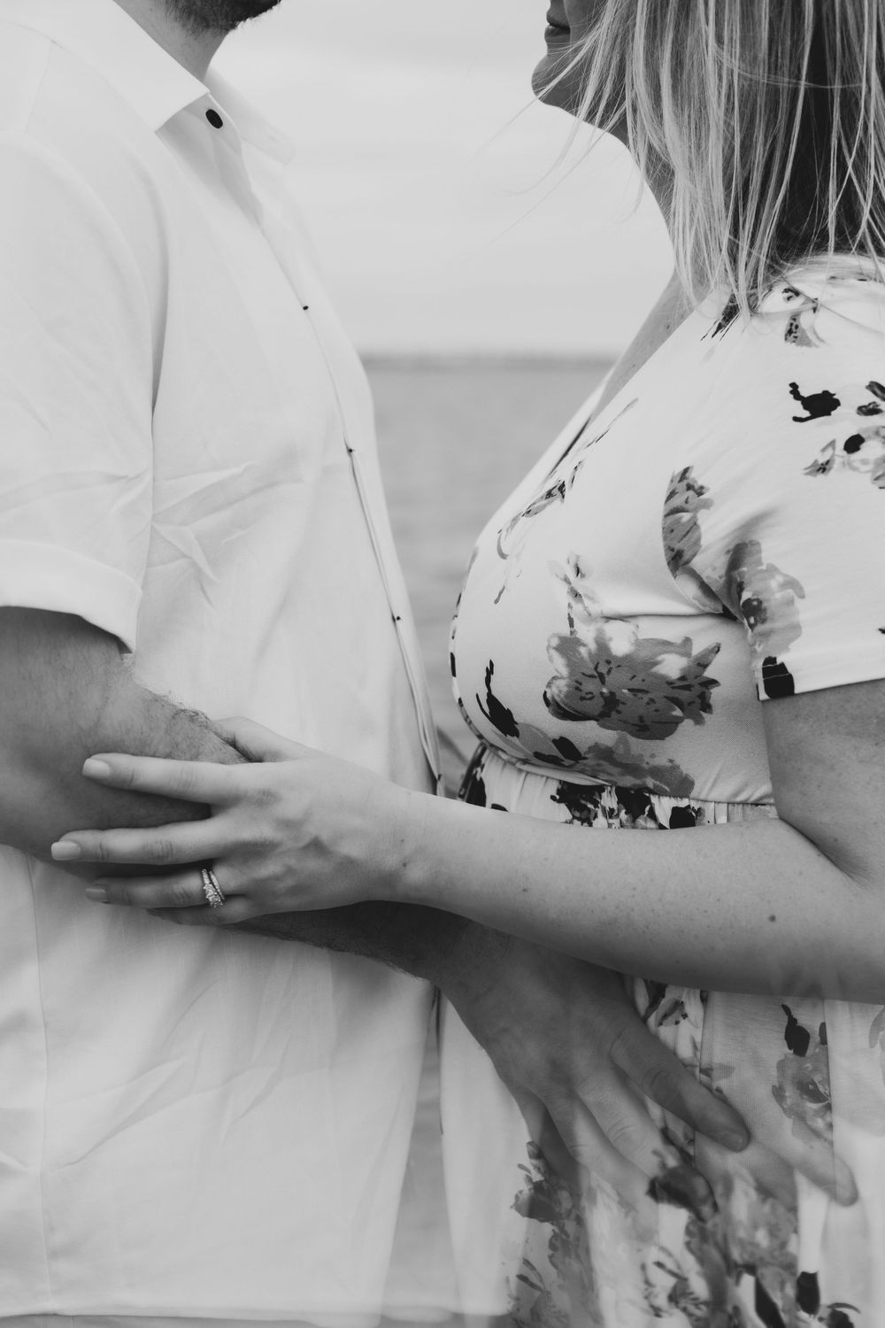 A black and white detail photo showing a couple embracing, with the woman wearing a floral dress and man in white shirt.