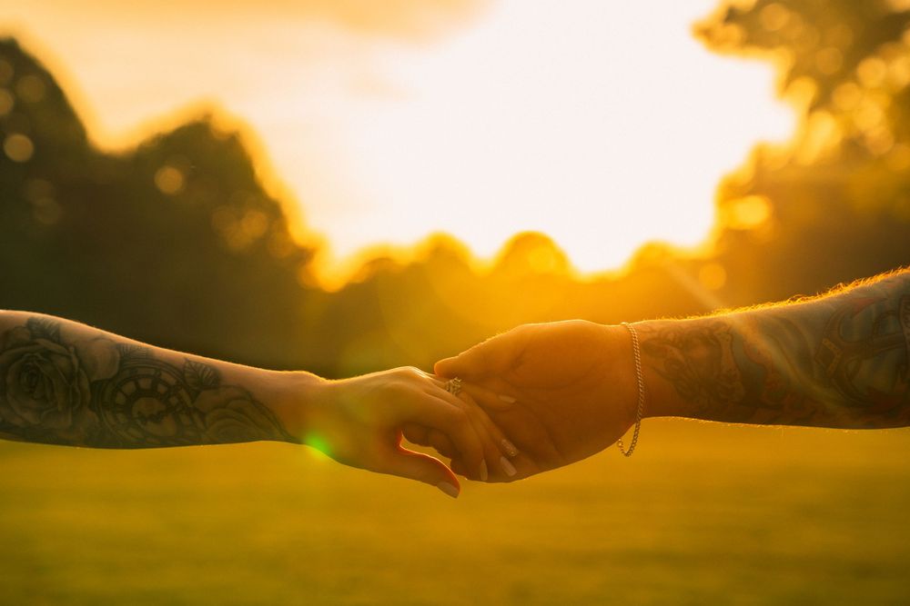 Hands gently coming together in prayer pose silhouetted against a golden sunset sky.