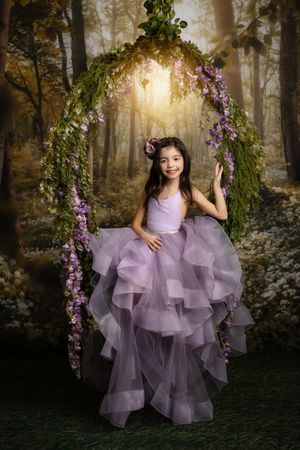 A dreamy forest scene with a purple tulle dress and floral decorations as sunlight streams through the trees.