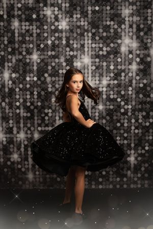 Elegant woman in black tulle dress poses gracefully against sparkly bokeh backdrop for artistic dance photos.