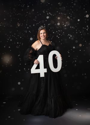Celebratory portrait in black gown holding large number 40 against dark sparkly background.