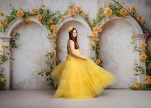 A bright yellow tulle ballgown stands out against stone archways adorned with climbing orange roses and greenery.