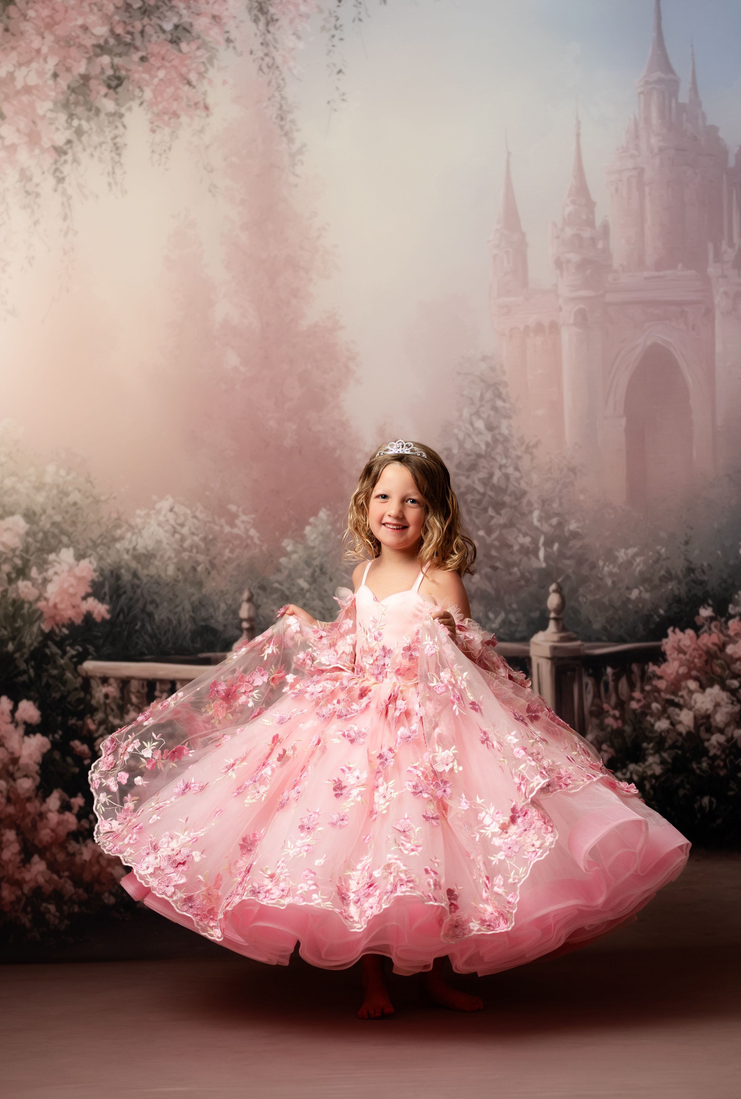 A young girl twirls in a pink floral ball gown with a tiara, posing before a dreamy castle backdrop.