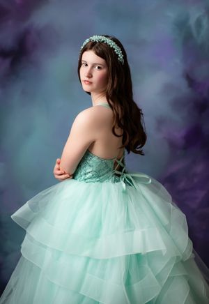 Elegant mint green ball gown with tiered tulle skirt against purple backdrop.