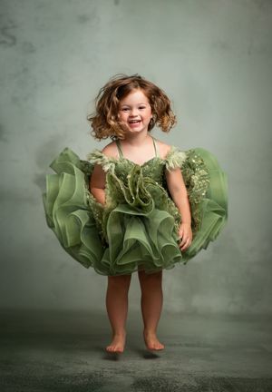 A whimsical portrait of a child wearing a ruffled green tutu dress against a gray studio backdrop.