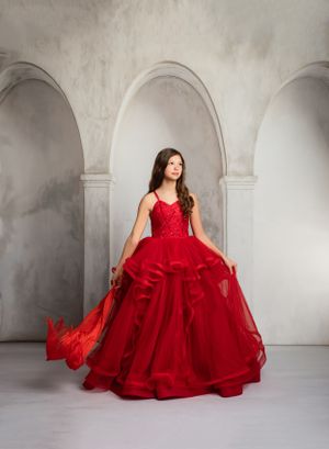 Elegant full-length red ball gown with corseted bodice and layered tulle skirt photographed against arched stone background.