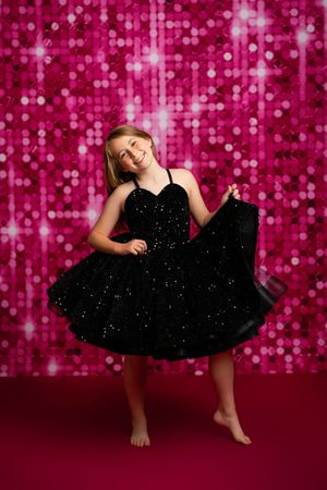 Dancing figure in black dress twirls against sparkly pink sequin backdrop creating joyful motion sequence.