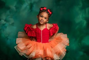 A dancer in a vibrant red and peach tulle tutu dress poses against a dreamy green backdrop.