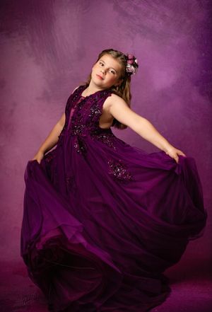 A young dancer twirls in an elegant purple sequined gown against a matching purple backdrop.