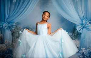 An elegant white flowing gown sparkles against a blue backdrop with sheer curtains and floral decorations.