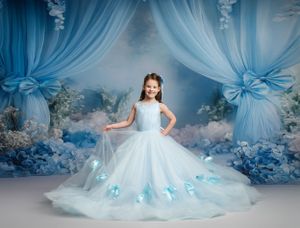 A flowing white and blue princess gown with tulle details in a dreamy blue backdrop with draped fabric and floral decor.
