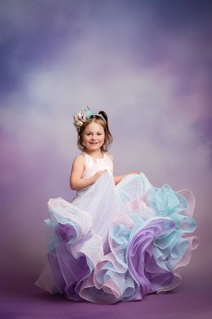 A child in a ruffled pastel dress poses gracefully against a purple backdrop in a professional studio portrait session.