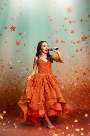 A collage showing a young child in an orange layered dress posing against a starry background with glowing orbs.
