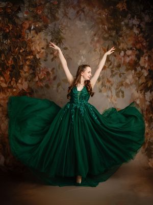 A flowing emerald green ballgown dress twirls dramatically against an autumn-toned backdrop in a series of artistic poses.