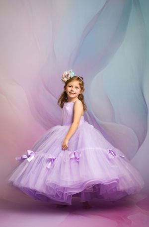 Beautiful lavender princess ball gown with tulle layers and bow accents against dreamy purple and blue backdrop.