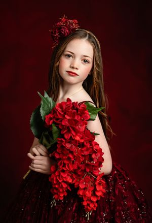 A dramatic portrait series against a deep red background featuring elegant poses with vibrant red flowers and a burgundy dress.