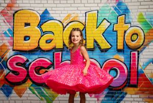 Vibrant back to school portrait with pink dress against colorful graffiti wall with yellow lettering.