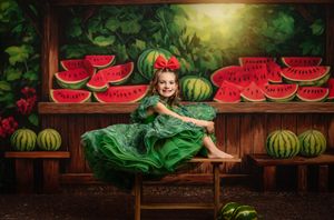 Whimsical scene with green-dressed subject posed among watermelon slices and whole watermelons on wooden shelves.