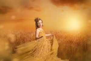 A flowing gold dress matches the warm sunset glow over a wheat field in this dreamy portrait photograph.