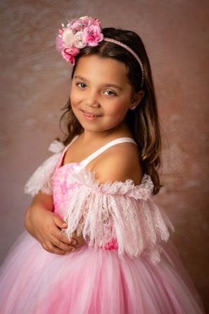 Portrait style photo with pink floral crown and tulle dress against brown backdrop.