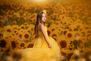 A person in a flowing yellow dress poses gracefully in a vibrant field of blooming sunflowers at sunset.