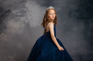 A figure in a flowing navy blue ballgown poses elegantly against a dramatic gray backdrop.