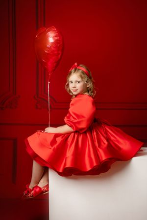 Stylish red dress photo with matching balloon against vibrant red wall backdrop.