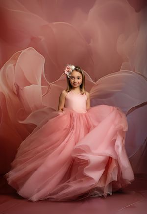 Young dancer in flowing pink tulle gown and floral headpiece poses elegantly against a soft rose-colored backdrop.
