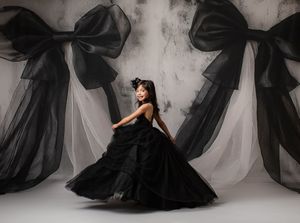 Elegant figure in flowing black tulle gown poses against white backdrop in artistic ballet-inspired movement sequence.