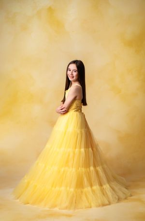 A flowing yellow tulle ball gown against a warm yellow backdrop creates an elegant portrait setting.