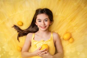 Bright yellow themed portrait with fresh lemons scattered on fabric and a matching yellow tank top.
