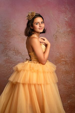 A model in a flowing peach tulle ballgown poses gracefully against a textured mauve backdrop.