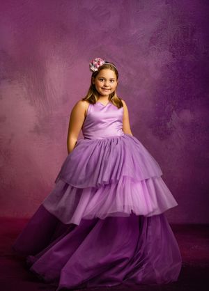 A young girl in a flowing purple tulle dress twirls gracefully against a dark purple studio backdrop.