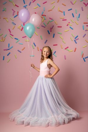 Series of photos showing a lavender tulle dress with confetti backdrop and balloons in pink studio setting.