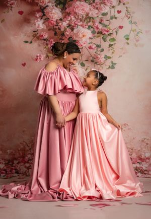 Two figures in flowing pink gowns pose against a romantic floral backdrop.