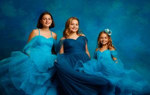 Three girls in matching blue tulle gowns pose elegantly against a blue studio backdrop.