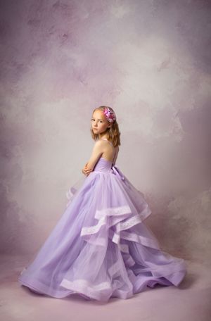 Elegant portrait featuring a flowing lavender ball gown against soft purple backdrop.