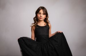 Elegant black sleeveless lace dress with full skirt photographed against grey studio backdrop.