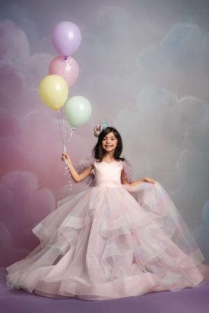 A magical portrait featuring a pink princess ballgown and pastel balloons against a dreamy clouded backdrop.